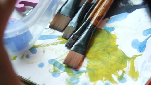 Close-up of assorted paintbrushes on a surface splattered with yellow and blue paint