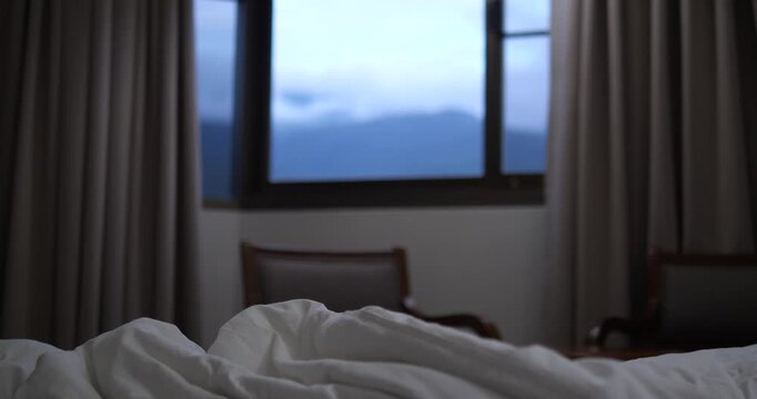First person POV of white duvet on bed with twilight mountain view