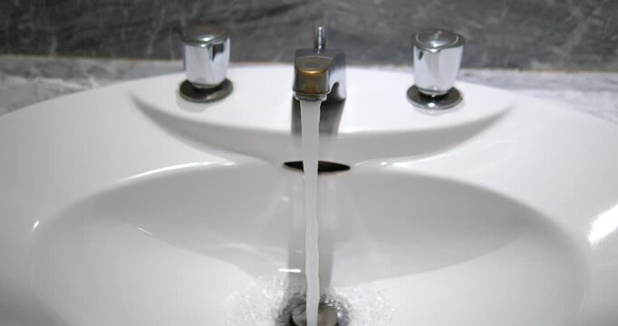 Water flowing from metallic faucet into clean white bathroom sink