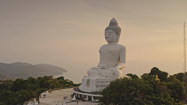 Big Buddha in Phuket, large white marble statue of Buddha, sitting peacefully on hilltop, panoramic view of tropical island, Andaman Sea and lush green hills at sunset soft light. Tourist attraction