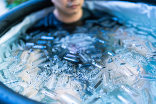 Young man immersed in an ice bath filled with ice cubes for cold plunge recovery. Ideal for sports recovery, wellness, muscle regeneration, biohacking, resilience, athletic performance, and healthy li