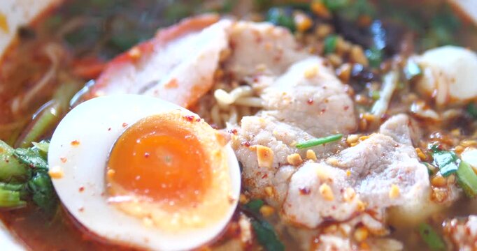 Close up of spicy Thai Tom Yum noodles with soft boiled egg and BBQ pork