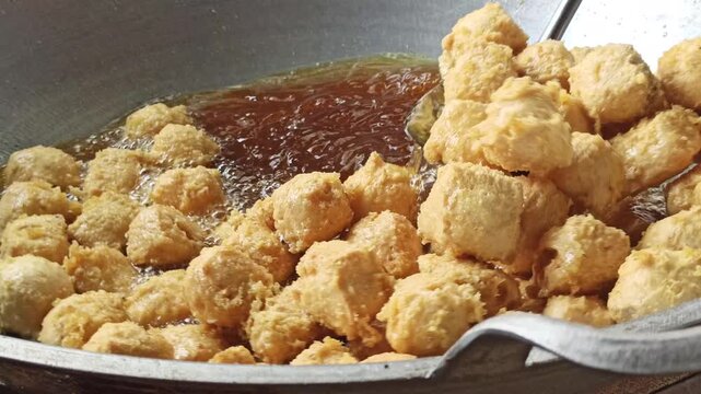 Fresh tofu being fried in hot oil during the preparation of crispy tahu kremes, showcasing the cooking process, golden texture, and traditional Indonesian culinary craftsmanship.
