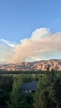 Vertical video of a massive wildfire smoke plume rising over mountains into the sky.