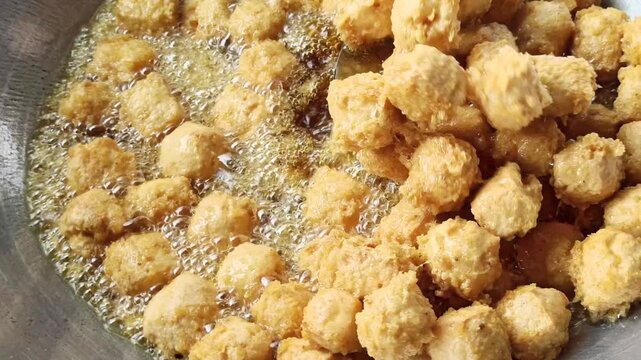 Fresh tofu being fried in hot oil during the preparation of crispy tahu kremes, showcasing the cooking process, golden texture, and traditional Indonesian culinary craftsmanship.