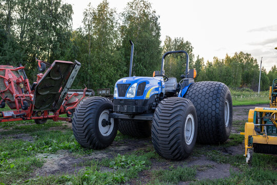 TYUMEN, RUSSIA - AUGUST 15, 2013: blue tractor with attached red harvesting equipment parked on field