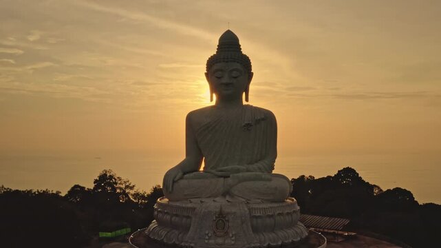 Big Buddha Phuket marble statue sitting in meditation, overlooking Andaman Sea landscape during a beautiful golden sunset, symbolizing peace and spiritual tranquility in Thailand. Aerial panorama