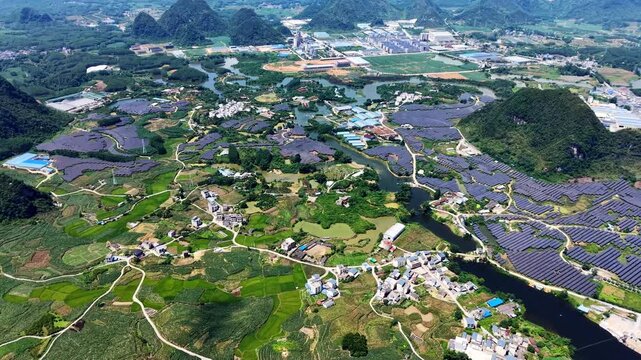 Cinematic aerial: Aerial view of solar farm interwoven with small river and farmhouses across sunny rural landscape