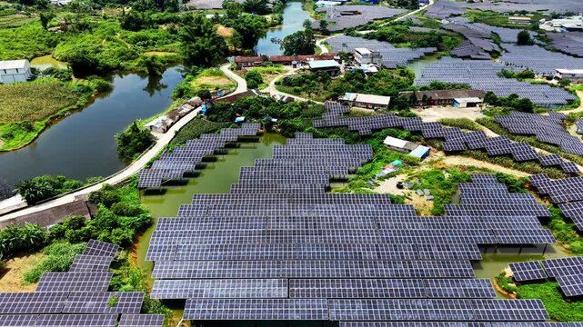 Cinematic aerial: Bird's eye view of photovoltaic panels nestled between farmland plots and tiny village clusters by river