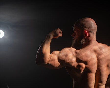 A male bodybuilder poses in shorts, showing off his back muscles.