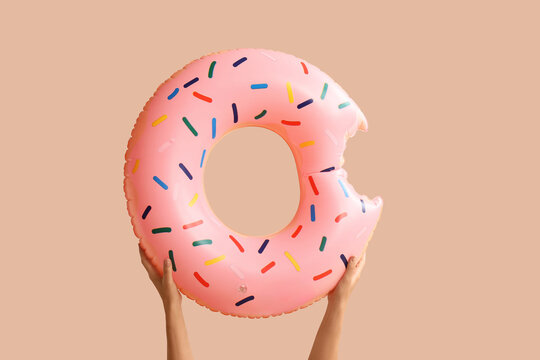 Hands holding a pink donut-shaped inflatable swimming ring with colorful sprinkles and a bite taken out, this summer vacation and pool party concept features a fun and playful design