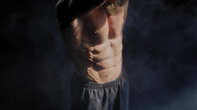 A male bodybuilder poses in shorts, showing off his muscles. Close-up of his chest and abs.