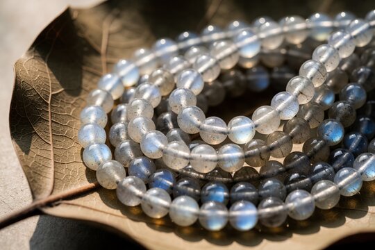 Strands of round labradorite beads display blue and grey iridescence. Gemstone jewelry rests on textured dried leaf. Natural mineral material offers subtle shimmering effect.