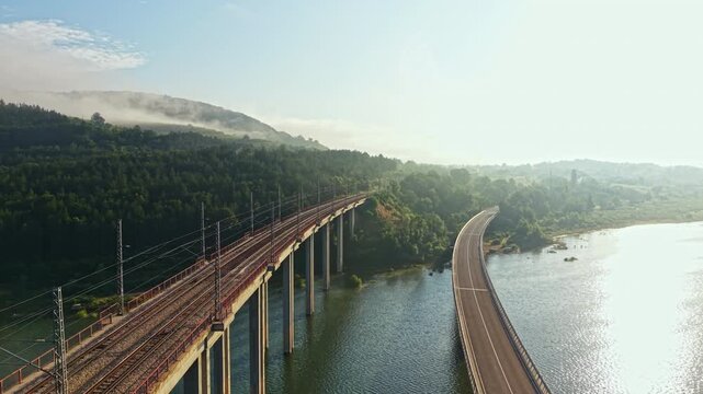 Twin elevated bridges cross reflective river landscape, with visible vehicle movement on both spans, dense flow on one side and lighter open lanes on other under warm sunlight, with bridge, traffic