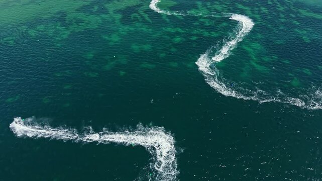 Racers on jet skis speed across open water in a race. The scene shows multiple jet skis carving paths through the surface, creating splashes and wake.