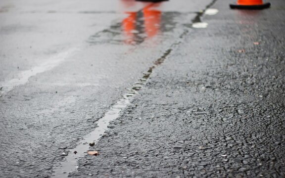 Wet asphalt road with pothole, traffic cones, and reflections in puddle after rain, Orange Traffic Cones and Barriers on Wet Asphalt Road in Rain - Street Maintenance