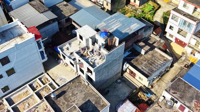 Cinematic aerial: Construction workers building a rural house with cement bricks on third floor in village center