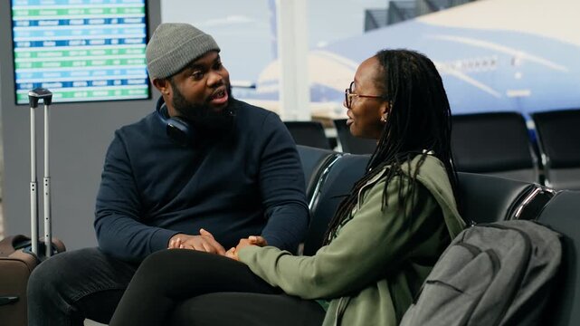 Black lovers talk about their journey while waiting for flight departure in an airport lounge, sharing a romantic moment and discussing leisure travel plans before their international flight.