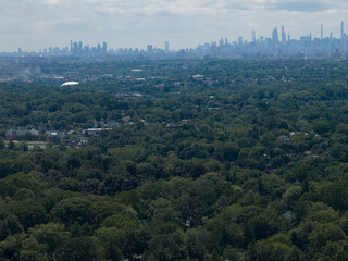 Fototapeta premium Aerial drone view of distant city skyline beyond a wooded suburban landscape in Bayberry Park, New Rochelle, New York