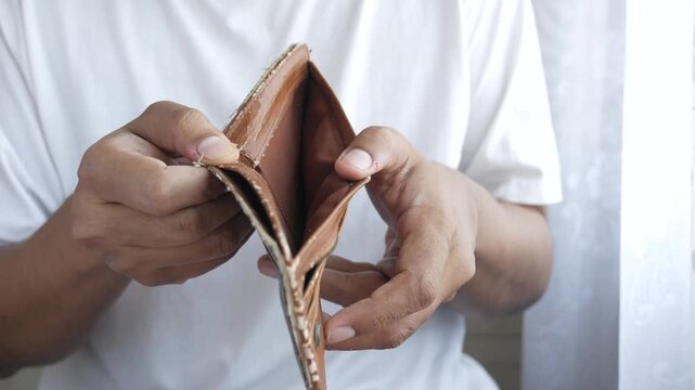 A person in a white t-shirt holds an empty wallet with both hands, showing the lack of money with a clear and static shot, symbolizing financial struggles and hardship