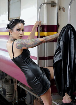Asian woman with tattoos wearing a black dress holding onto handrails while stepping onto a train