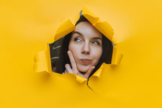 A young girl puts her hand to her cheek and listens, her mouth covered, her eyes narrowed slyly with suspicion.A ragged hole in the paper background.Eavesdropping, espionage, gossip, and the tabloids.