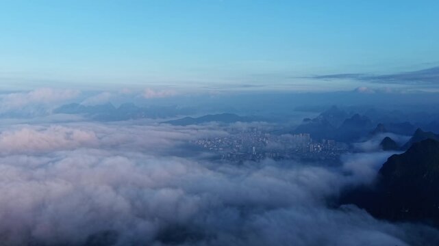 Cinematic aerial: Misty karst peaks surrounding a county town with river and morning fog at sunrise