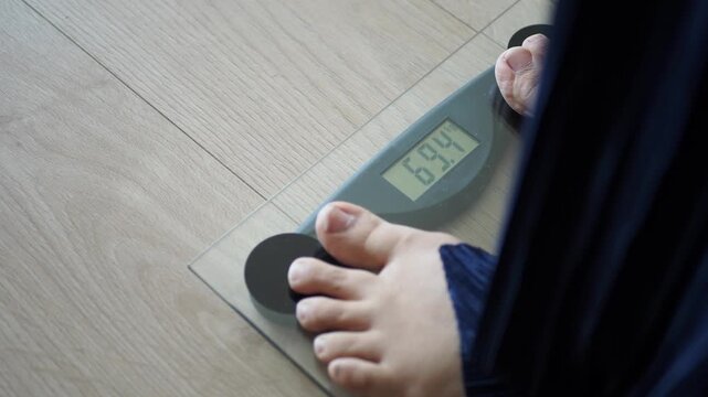 Close up of woman feet stepping on digital glass scale to measure weight indoors on wooden floor