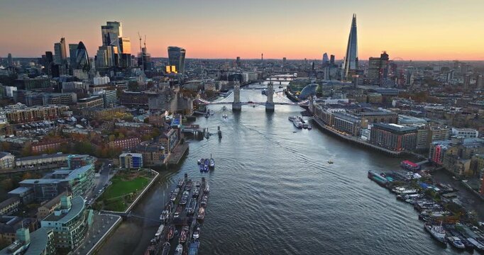 Travel and explore London. River Thames and the iconic Tower Bridge spanning the cityscape with various boats navigating the waterway. Aerial drone flight over modern England capital city skyline