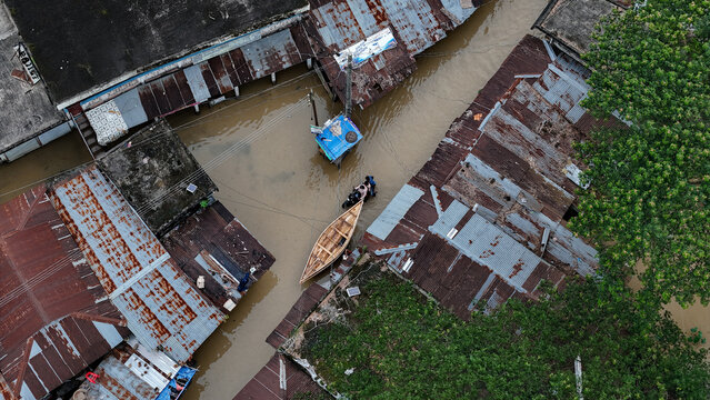 Osmaninagar, Sylhet Division, Bangladesh - 07 May 2024: Aerial view of flooded houses with corrugated metal roofs and a small wooden boat navigating through the murky water.