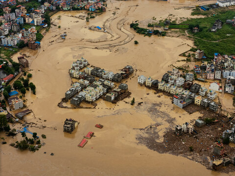 Nepal - 28 September 2024: Aerial view of a flooded urban area with muddy brown floodwaters surrounding residential buildings and debris.
