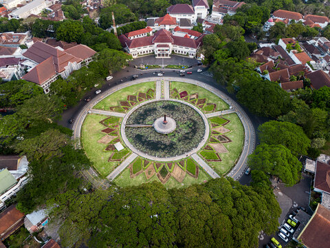 Malang, Indonesia - 25 July 2026: Aerial view of Alun Alun Malang, featuring its circular central pond, geometric garden beds, lush trees, and surrounding historic buildings.