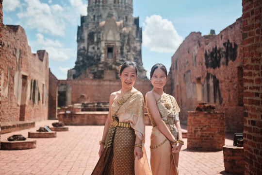 Asian family, mother and child dressed in Thai traditional outfit with cheerful smiles and looking at camera, holiday travel in Ayutthaya, Southeast Asia, ancient ruins heritage,  tourist destination.