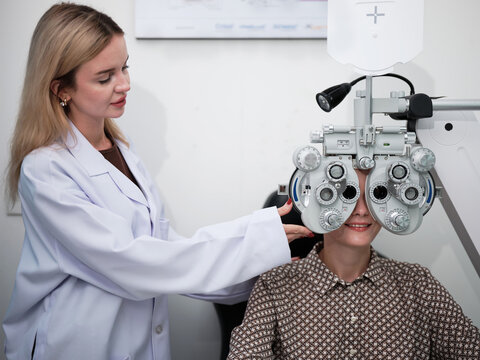 White female patient eye exam with phoropter equipment, vision and eyesight improvement by expert optometrist woman, diagnostic for eyeglasses lens, professional technology services in optical clinic.