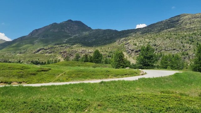 Small alpine road on Simplon Pass in Valais, Switzerland, winding through lush green mountain landscapes. A peaceful hiking paradise beneath clear blue spring skies in the heart of the Alps