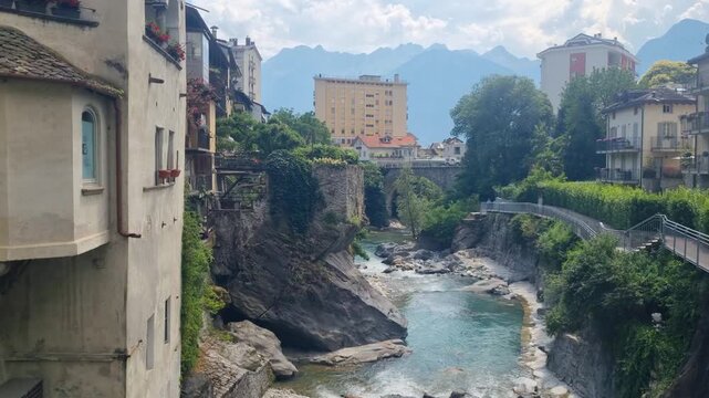 Scenic view of Chiavenna, Lombardy, Italy, the Mera River, lush Mediterranean vegetation, and the dramatic Rhaetian Alps, highlighting the charm of this historic Alpine town
