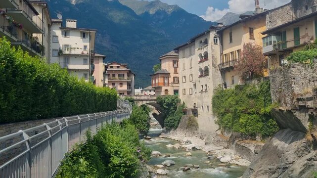 Stunning view of Chiavenna in Lombardy, Italy, charming riverside architecture, the flowing Mera River, Mediterranean greenery, and the rugged Rhaetian Alps surrounding this historic Alpine town