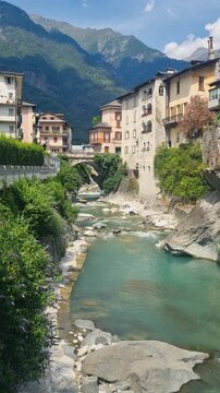 Vertical view of Chiavenna, Lombardy, Italy, revealing historic riverside buildings along the Mera River, Mediterranean vegetation, and the dramatic Rhaetian Alps, capturing its unique charm