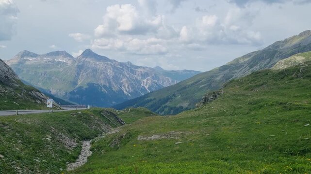 Panoramic view from the Swiss border at Spl&uuml;gen Pass in Graub&uuml;nden, overlooking a dramatic high-altitude Alpine landscape with rugged mountain terrain, lush green meadows, and breathtaking scenery
