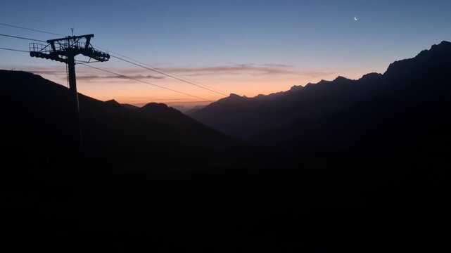 Last light fades over Hahnenmoos, Adelboden, Switzerland, as the silhouettes of a gondola lift and Alpine mountain range stand against the evening sky. A peaceful twilight scene in the Swiss Alps