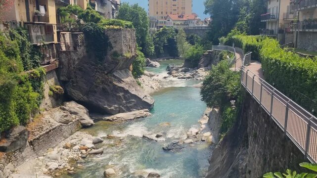 Scenic summer view of Chiavenna, Lombardy, Italy, featuring the Mera River, lush Mediterranean vegetation, and the charming historic Alpine town nestled in the Valchiavenna valley