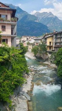 Vertical view of Chiavenna, Lombardy, Italy, with the Mera River flowing beneath the dramatic Rhaetian Alps, showcasing the timeless charm of this historic Alpine town