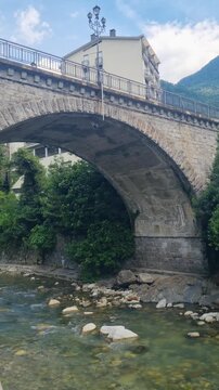 Historic stone bridge spanning the Mera River in Chiavenna, Lombardy, Italy, framed by the dramatic Rhaetian Alps. A scenic Alpine landmark blending architecture, nature, and mountain scenery