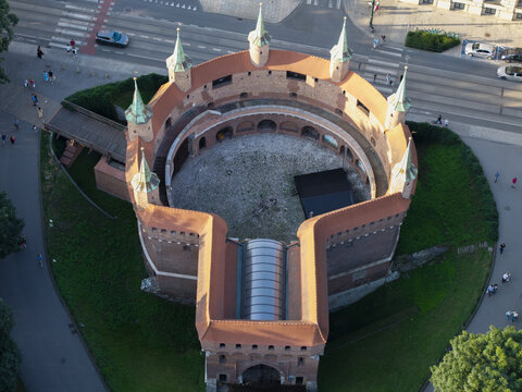 Krakow, Poland - 20 July 2026: Aerial view of the historic Krakow Barbican, a medieval fortified outpost with red brick walls and towers, surrounded by green parkland and city streets.