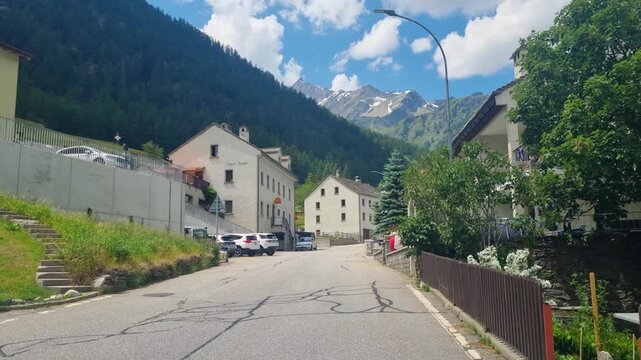 Walking through the main street of Simplon Dorf, Switzerland, a charming alpine village where travelers stop along the route between Switzerland and Italy. Sunny mountain scenery in the remote village