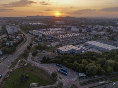 Krakow, Poland - 13 July 2026: Aerial view of an industrial area with warehouses, a bus depot, and tram tracks during a golden sunset.