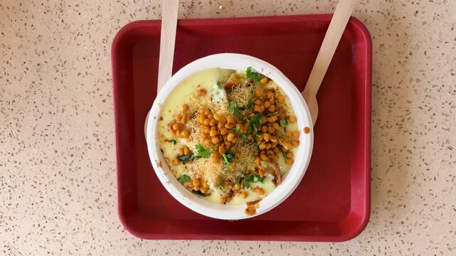 indian dahi chaat topped with sev and boondi served in disposable bowl on food tray