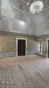 Historic interior with detailed Islamic tiles, carved plaster arches, and chandelier-lit dome in Zawiya of Sidi Sahib also known as the Mosque of the Barber in Kairouan, Tunisia.