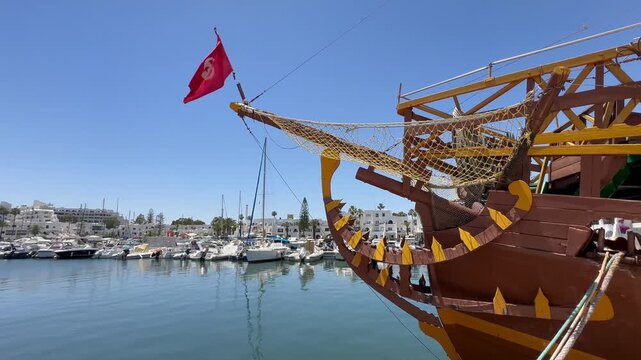 A traditional wooden tour boat with a Tunisian flag sits in a calm marina beside modern yachts and white waterfront buildings. Tunisia,