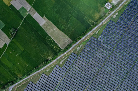 Rangpur, Bangladesh - 04 October 2025: Aerial view of Teesta Solar Power Plant featuring rows of photovoltaic panels adjacent to lush green agricultural fields and a rural road.